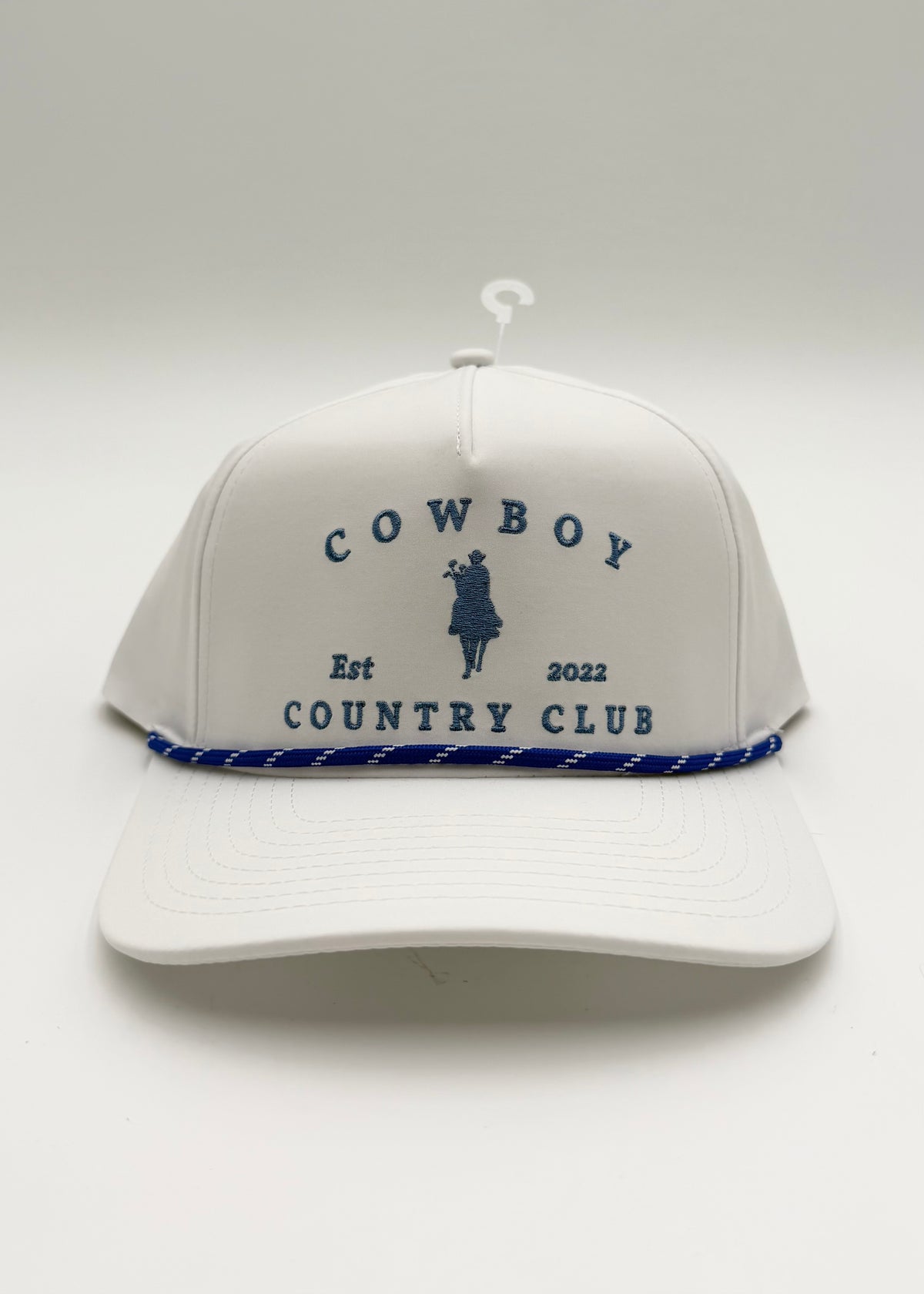A white baseball cap with a blue rope detail along the brim and navy blue embroidered text reading 'COWBOY COUNTRY CLUB' with a cowboy silhouette, shown on a light gray background.