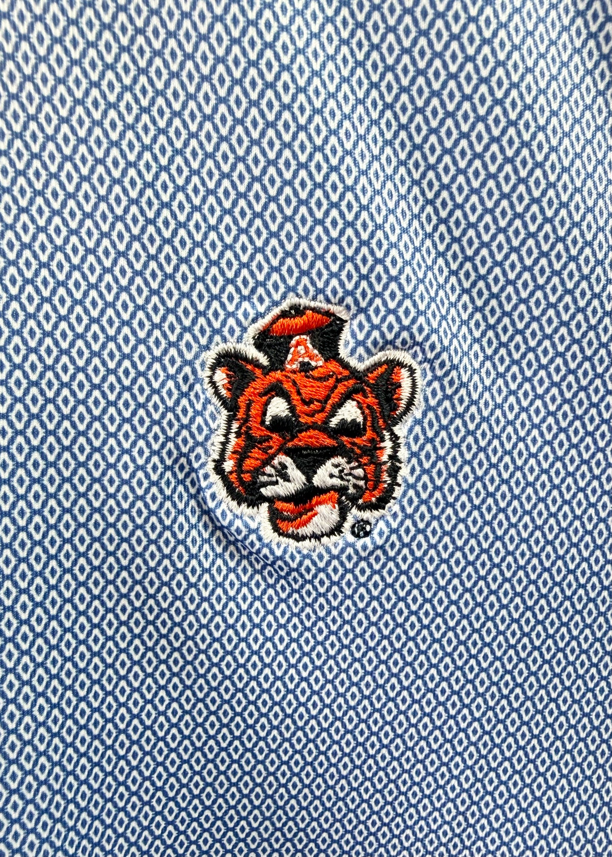 Close-up of a light blue textured polo shirt featuring an embroidered tiger mascot logo with a white 'A' on its forehead.