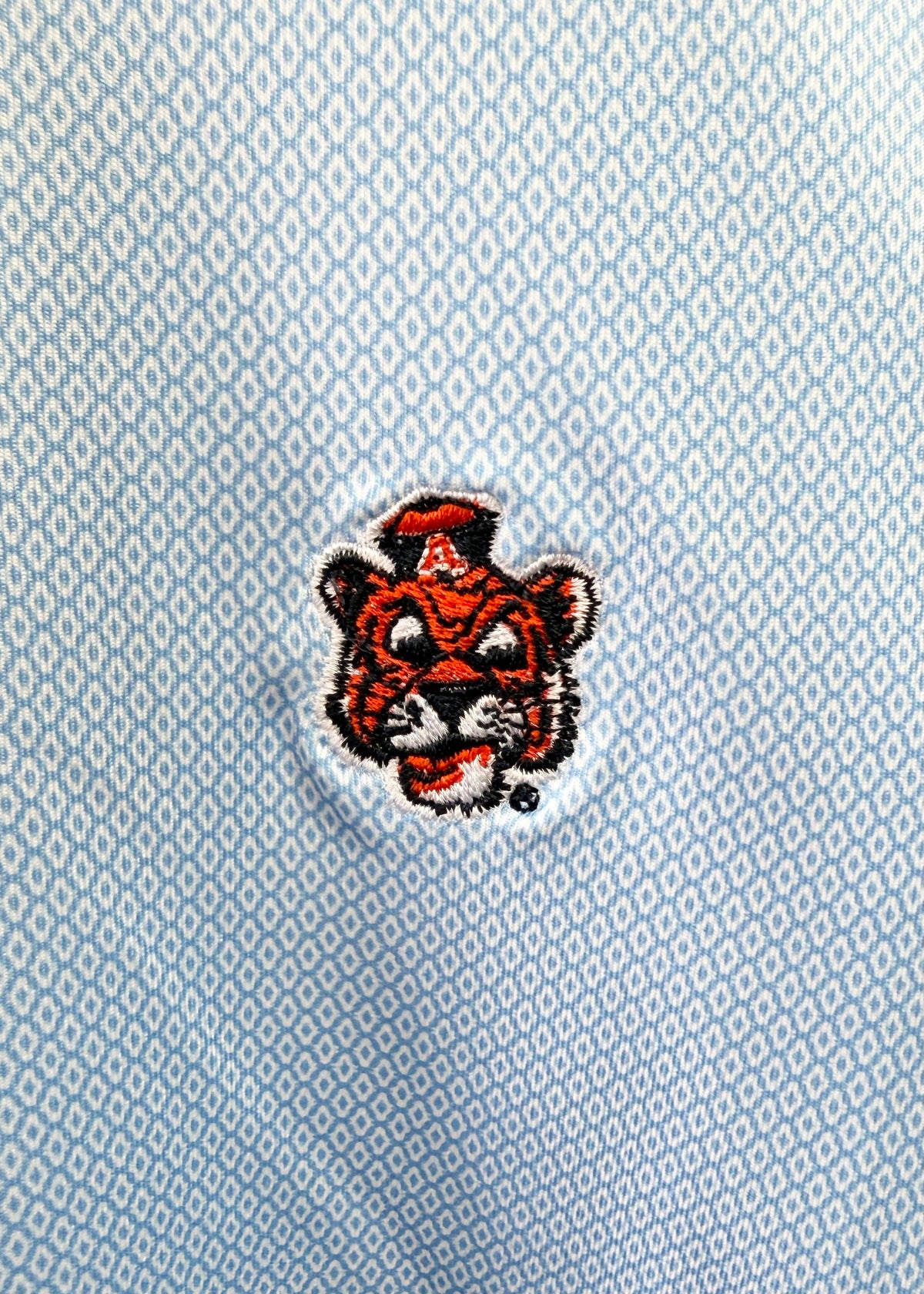 A close-up of a light blue textured fabric featuring a small embroidered tiger mascot patch with a red and black design and a white border.