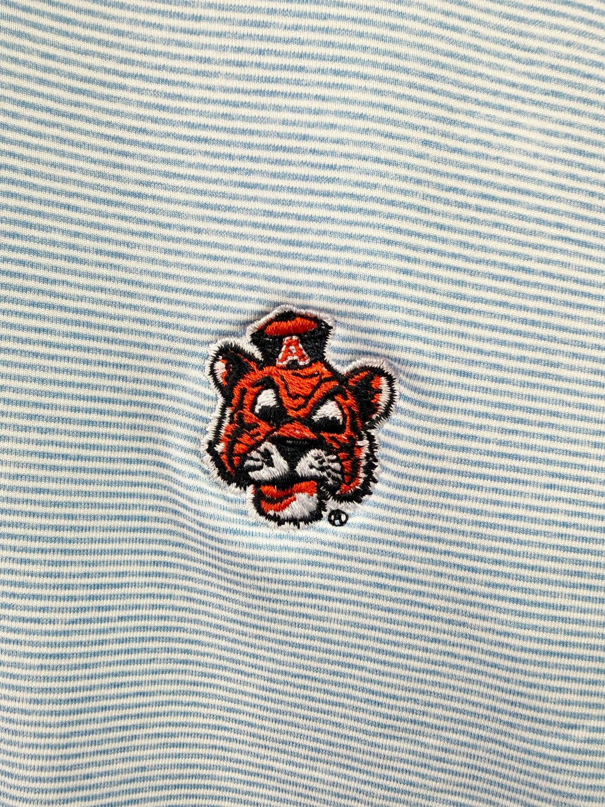 Close-up of a light blue and white striped fabric with an embroidered tiger mascot patch featuring a red letter A on its hat.