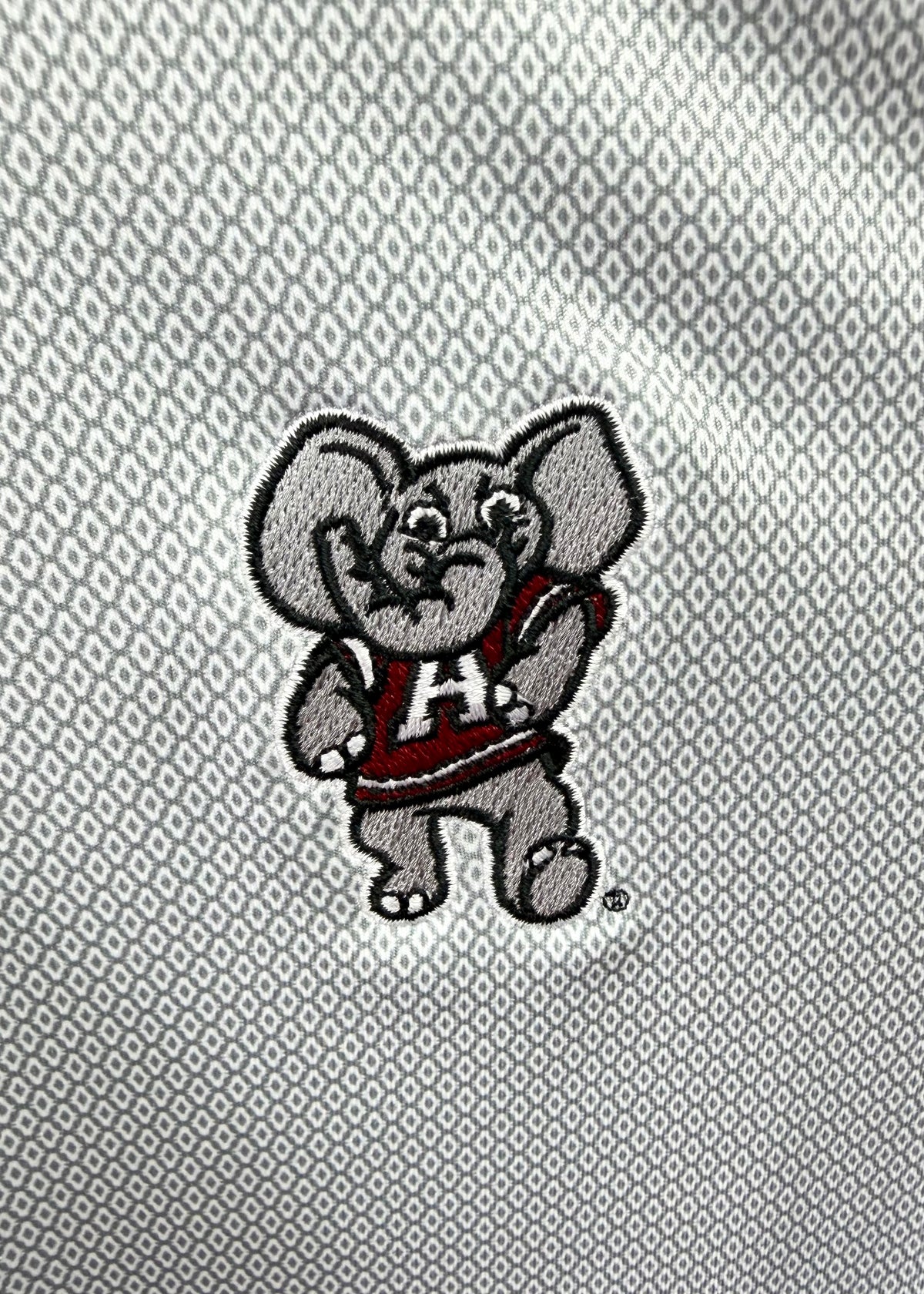 Close-up of a gray embroidered elephant mascot patch with a red and white 'A' jersey, placed on a textured gray fabric background.