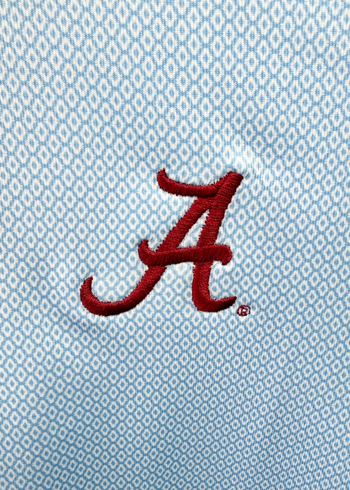 Close-up of a light blue and white patterned fabric with a red embroidered script letter 'A' logo.