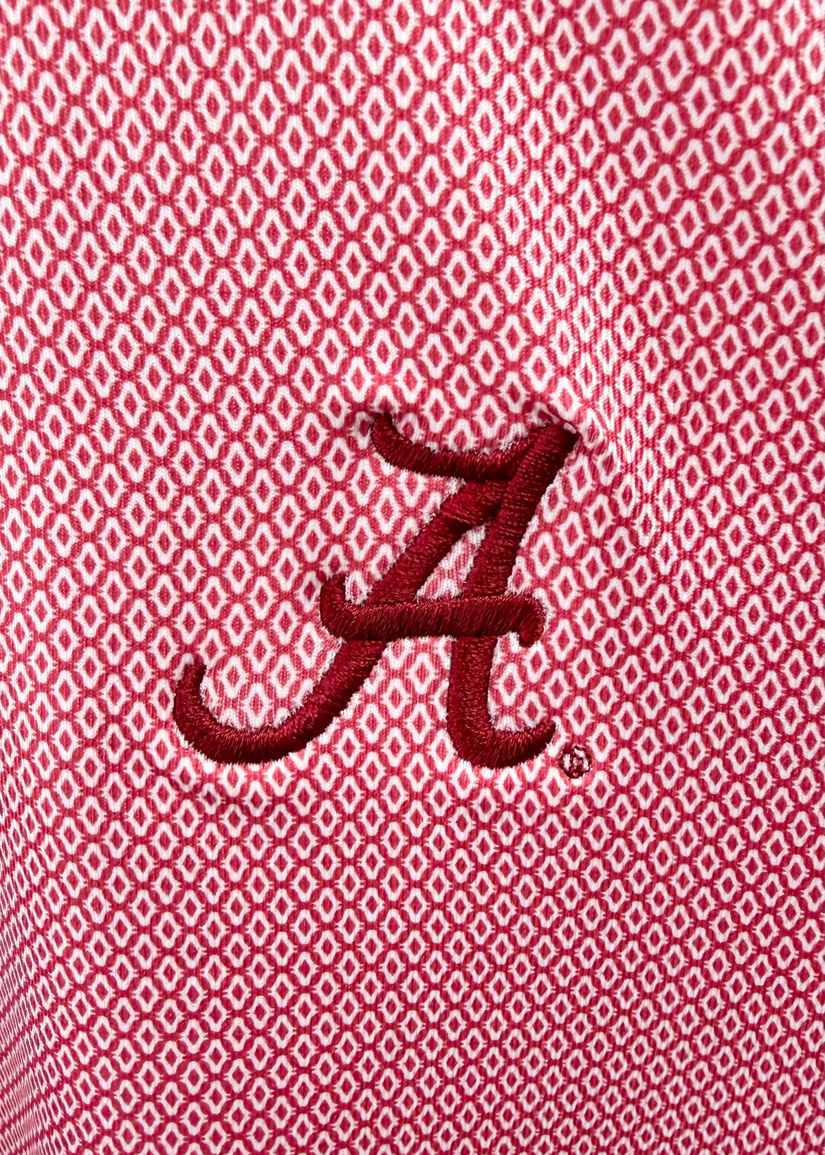 Close-up of a red embroidered Alabama 'A' logo on a red and white micro-patterned fabric background.