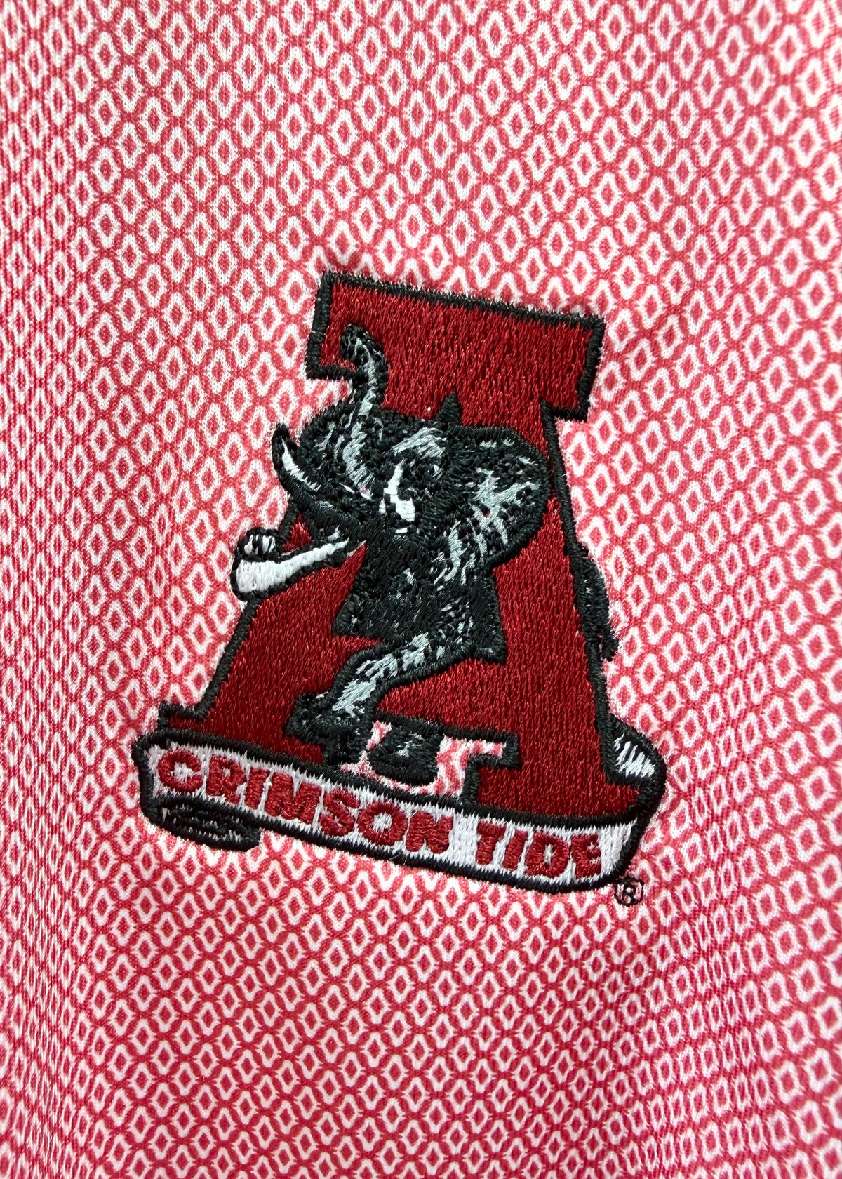 Close-up of a red embroidered Alabama Crimson Tide logo patch on a red and white patterned knit fabric background.