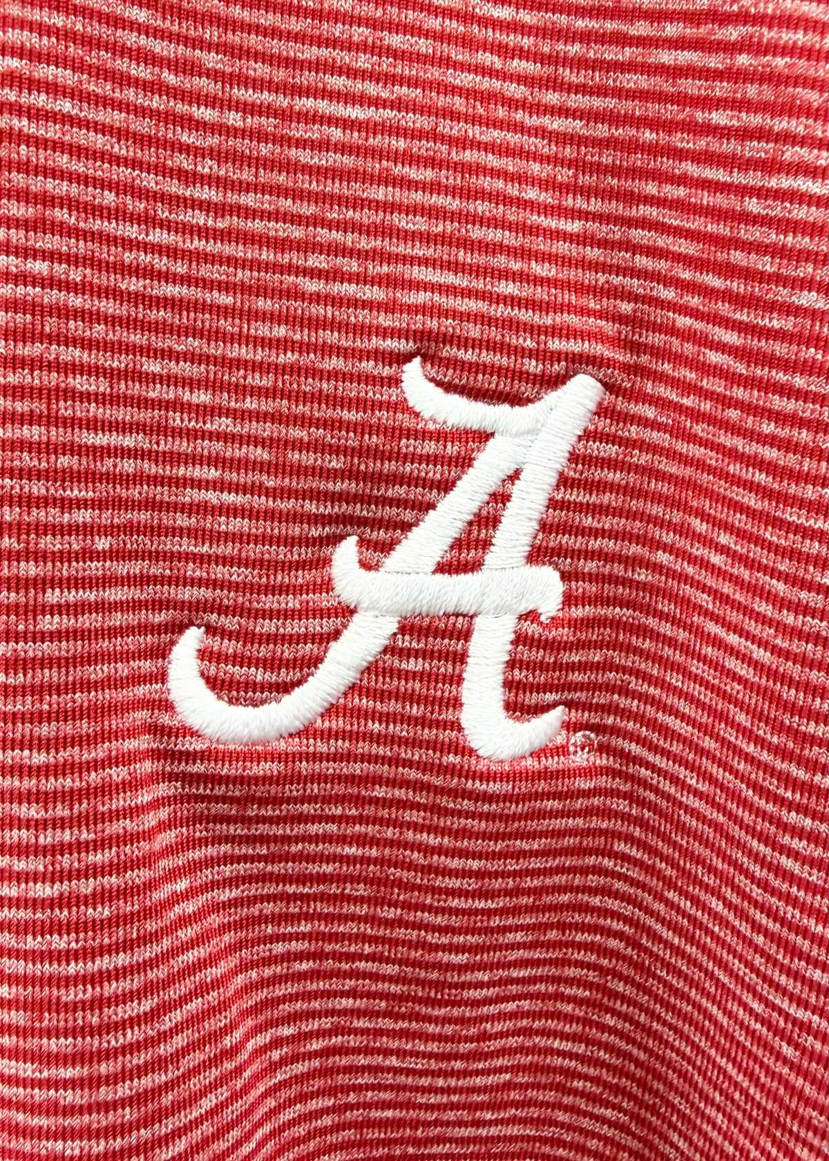 Close-up of a red and white striped knit fabric with a white embroidered script letter A logo.