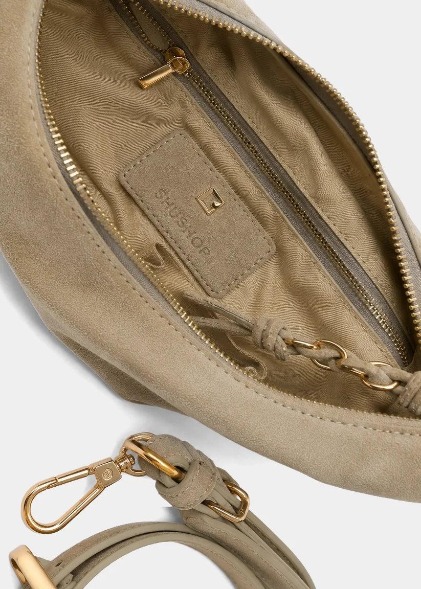 Close-up of a taupe suede shoulder bag with gold-tone hardware, showing the interior zip pocket with a branded interior label and a matching detachable strap clasp.