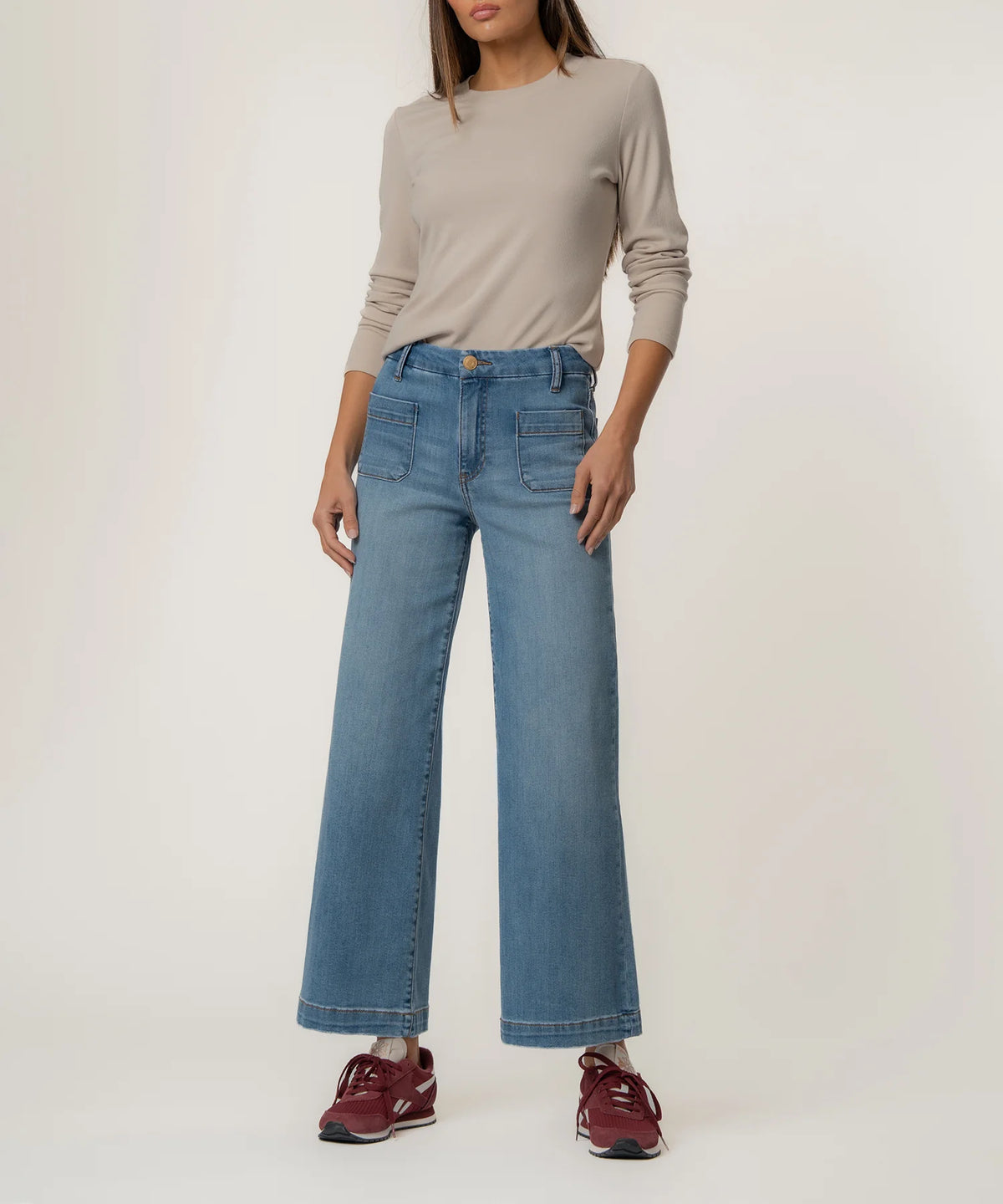Person wearing a beige long-sleeve top and blue jeans on a white background