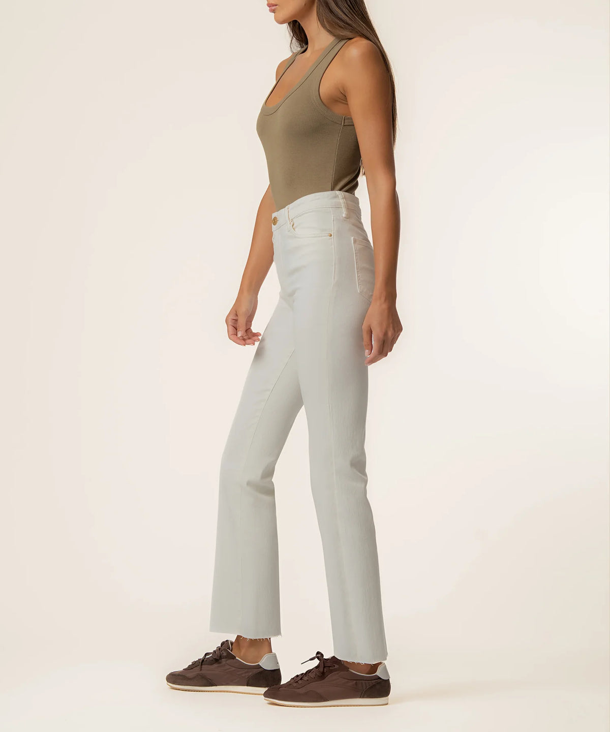 A woman modeling a pair of light gray high-waisted, wide-leg jeans with an olive green tank top and brown suede shoes, shown from the side against a plain off-white studio background.
