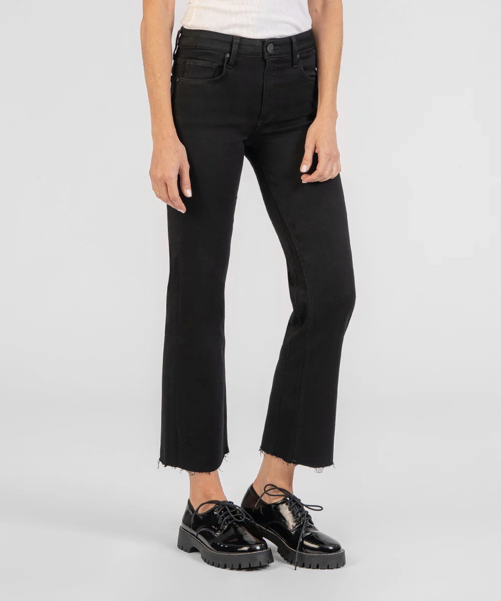 A model wearing black cropped flare jeans with a raw hem, paired with black patent leather lace-up shoes, shown against a light gray studio background.