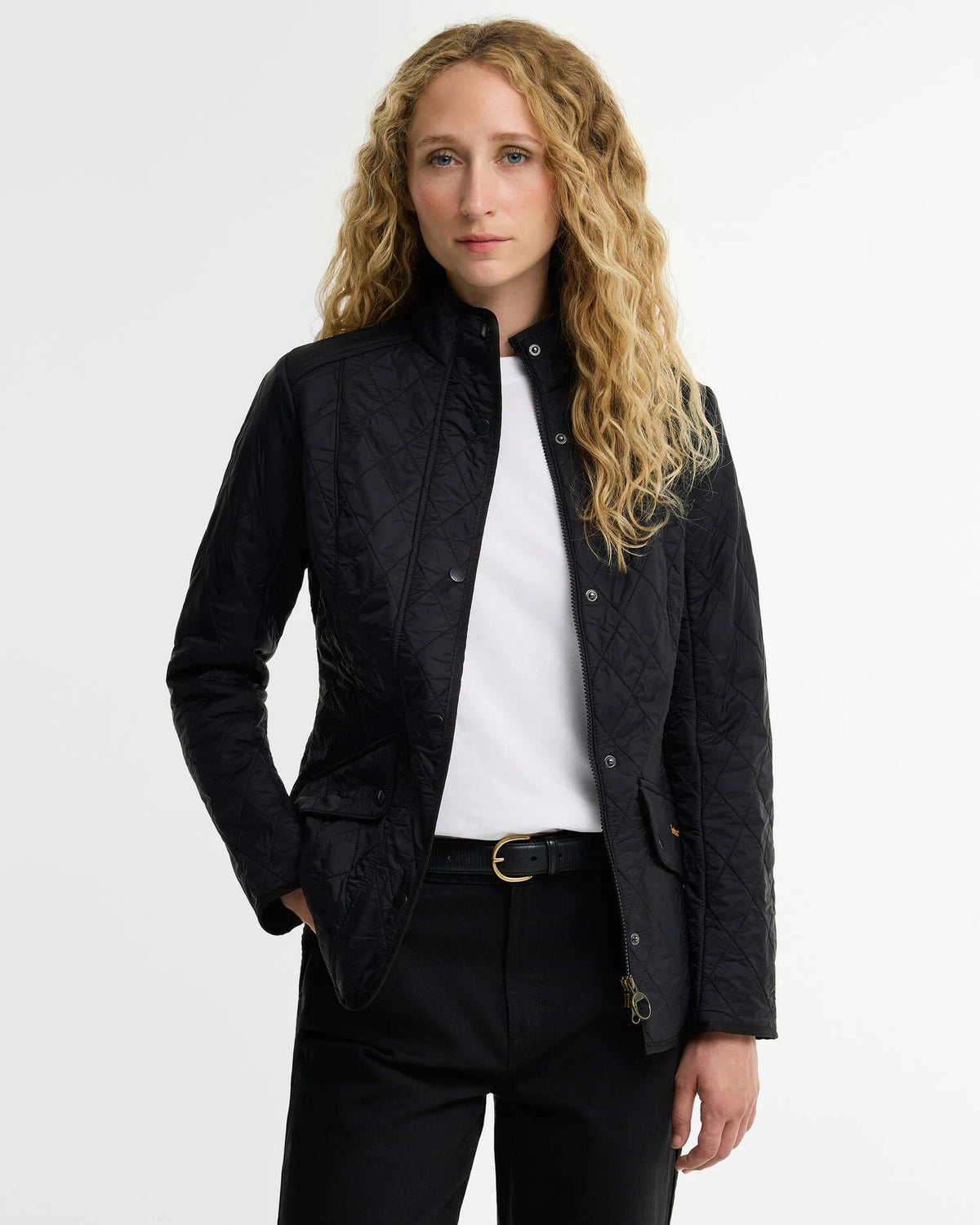 A woman modeling a black quilted jacket over a white top and black trousers against a plain light gray studio background.