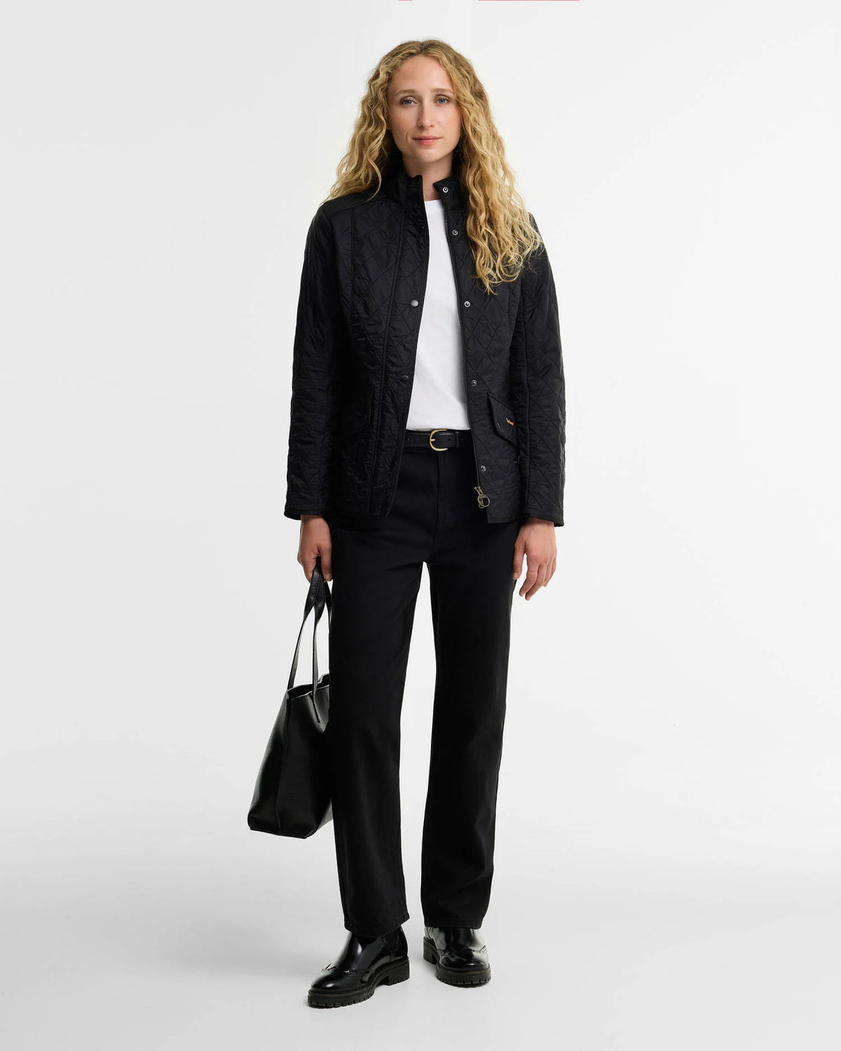A woman modeling a black quilted jacket over a white top and black trousers against a plain light gray studio background.