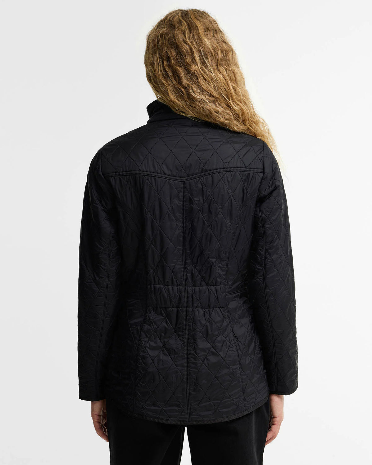 A woman viewed from the back wearing a black quilted jacket with a geometric diamond pattern, set against a plain white studio background.