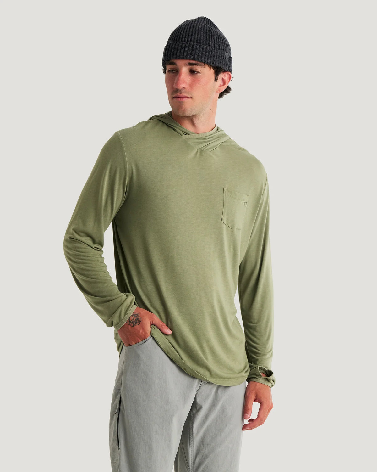 Man wearing a green long-sleeve shirt and gray pants on a light gray background