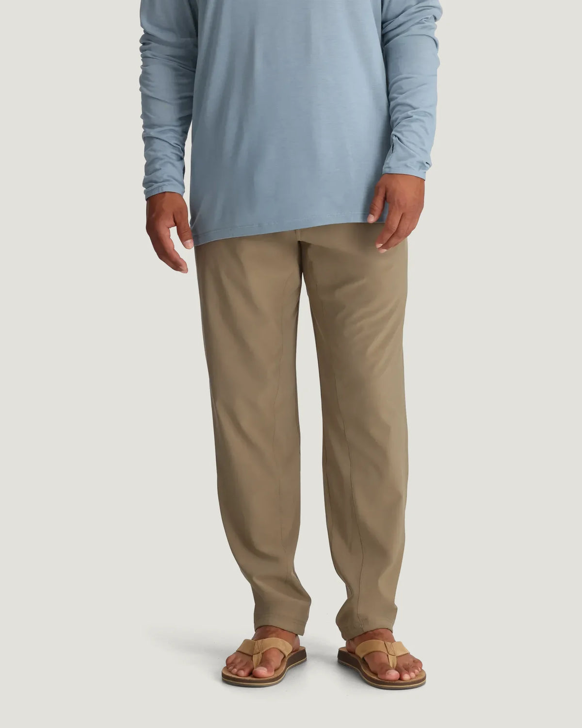 Person wearing a light blue long-sleeve shirt and beige pants on a plain background