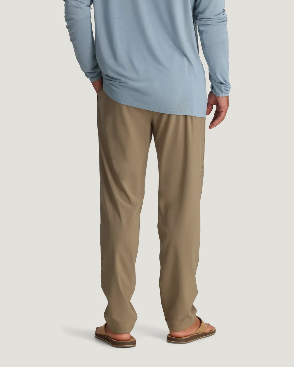 Person wearing a light blue long-sleeve shirt and beige pants on a white background