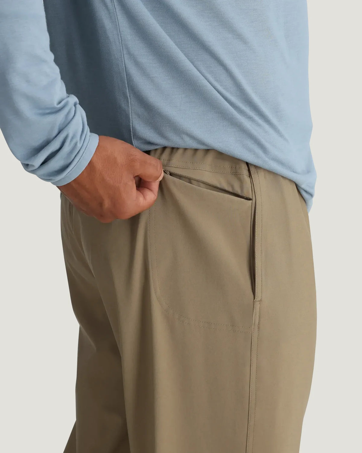 Person wearing beige pants and a light blue shirt on a plain background