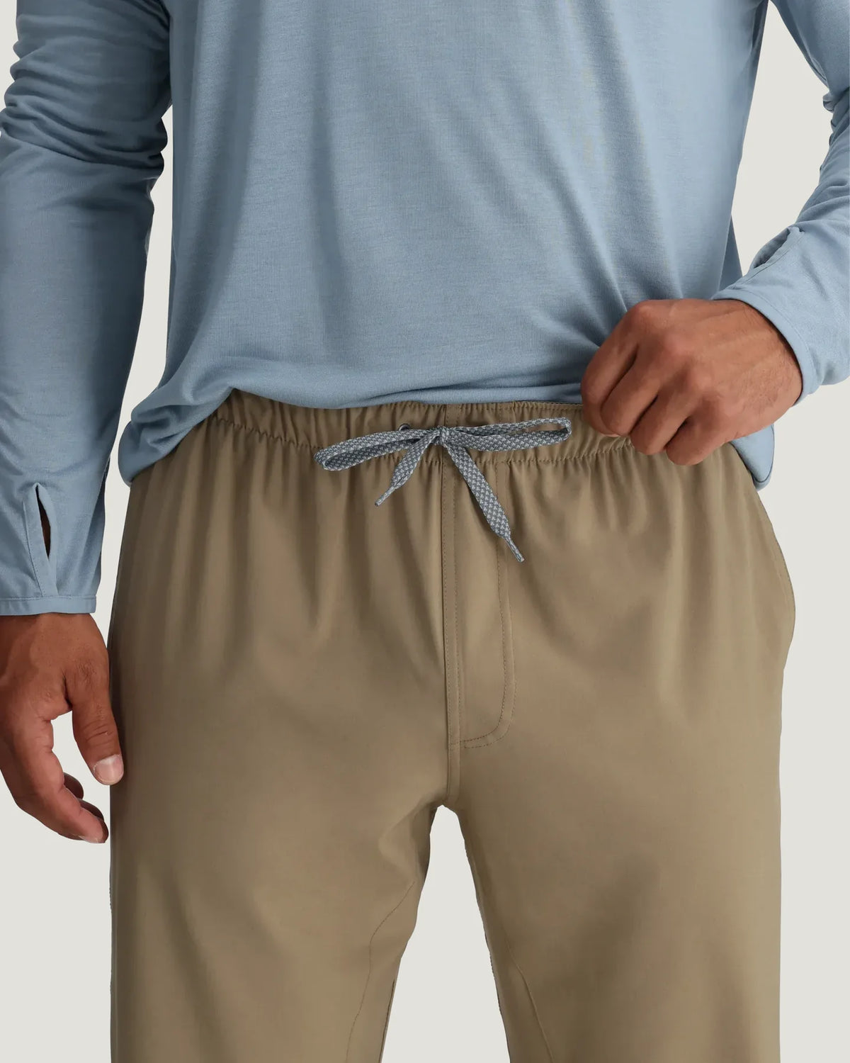 Person wearing a light blue long-sleeve shirt and beige pants on a neutral background