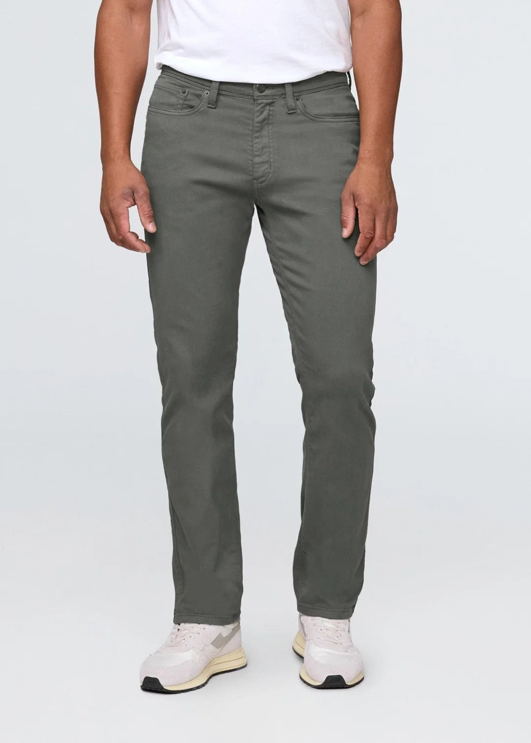 Man wearing a white t-shirt, gray pants and white shoes standing in front of a white background. 
