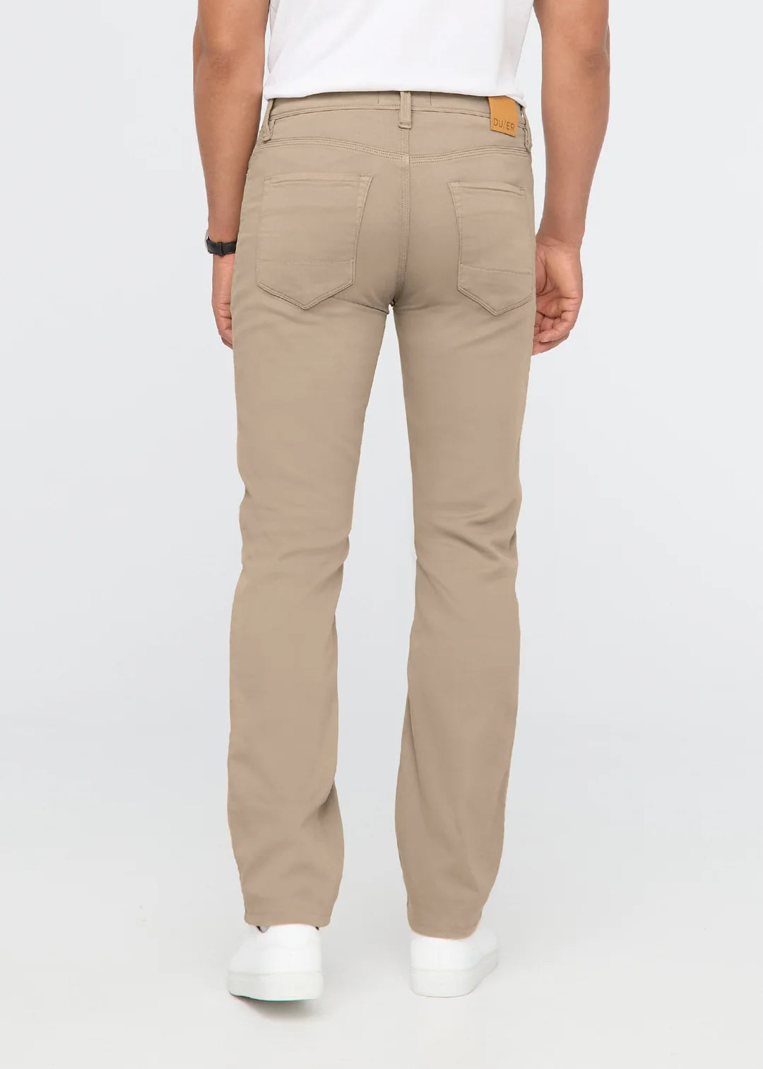 Back view of a man wearing a white t-shirt, khaki pants and white shoes standing in front of a white background. 