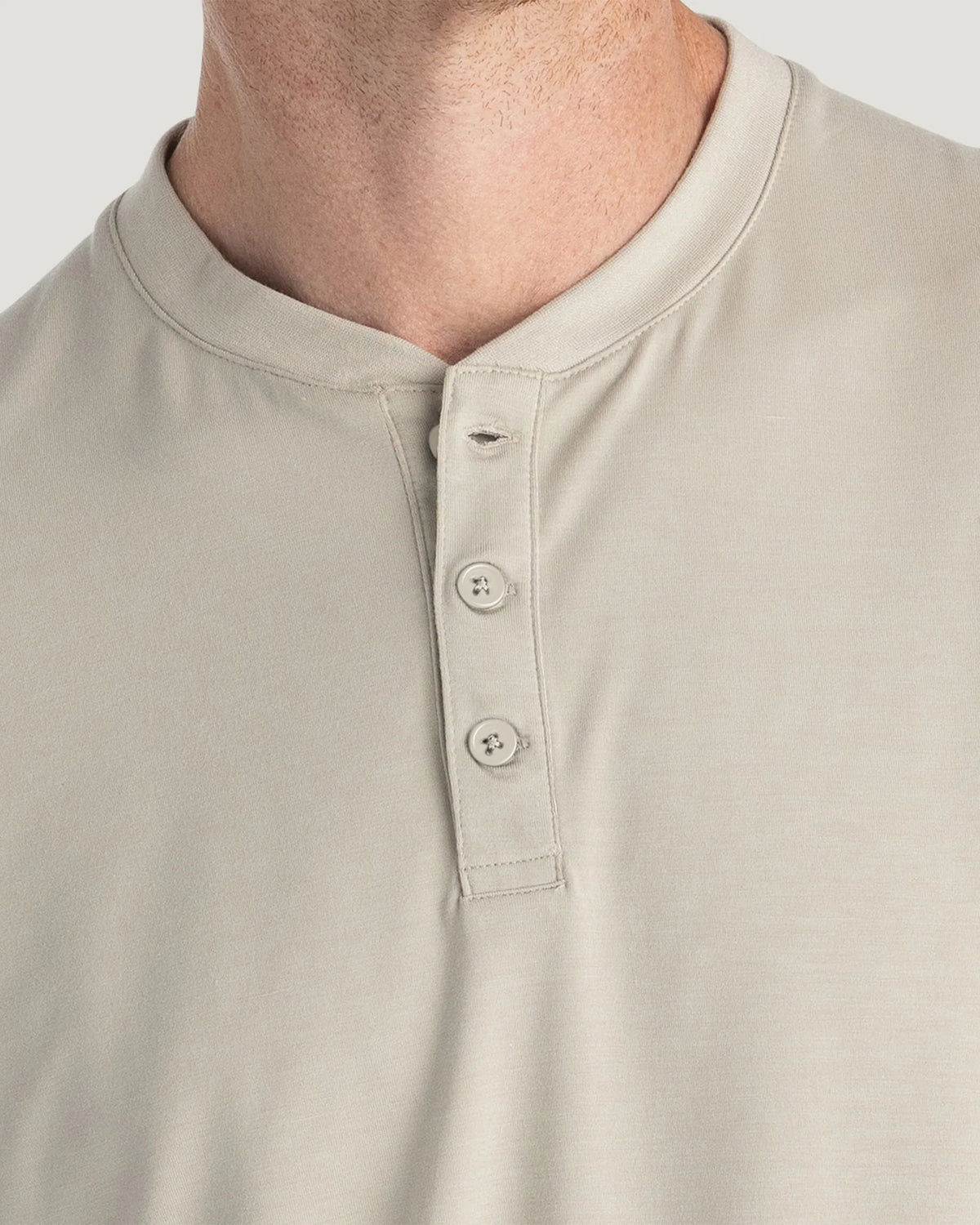Close-up of a man wearing a light beige henley shirt, showing the collar, three-button placket, and fabric texture.