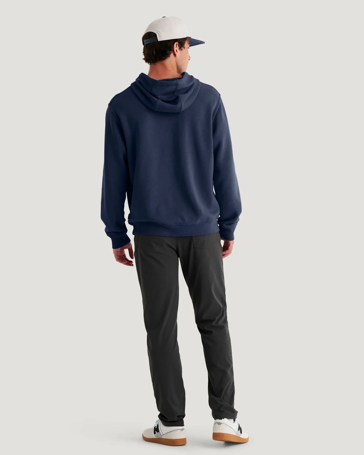 Person wearing a navy hoodie and dark pants on a light gray background