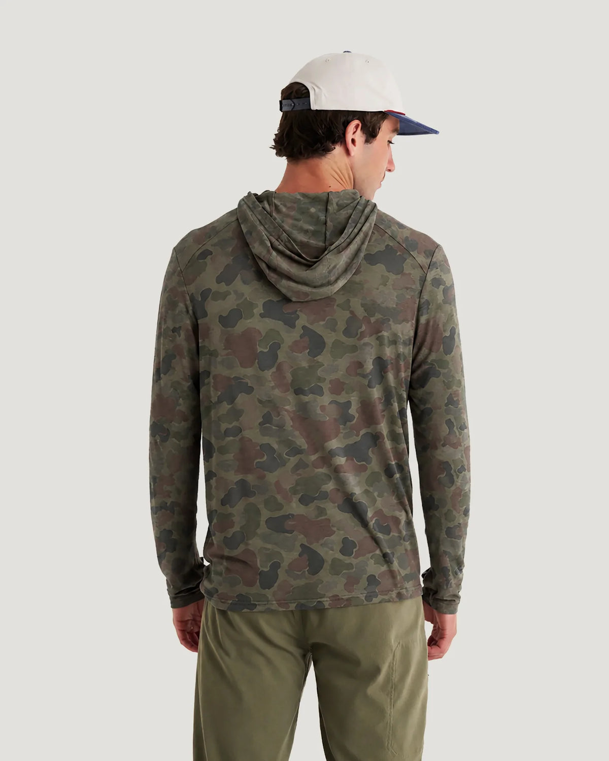 Person wearing a camouflage hoodie and cap on a plain background