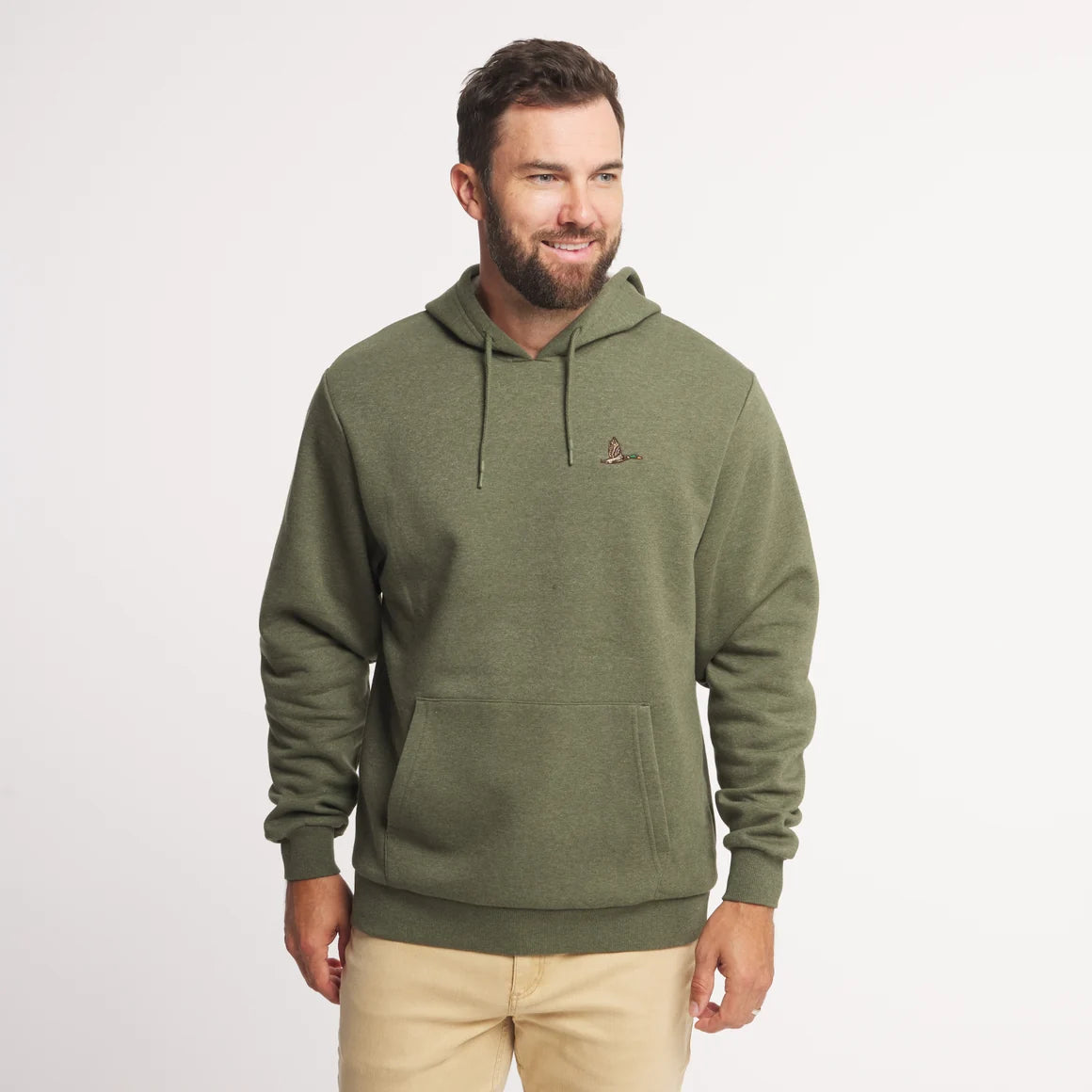 A man wearing an olive green pullover hoodie with a small embroidered logo on the left chest, paired with beige pants, standing against a plain white studio background.