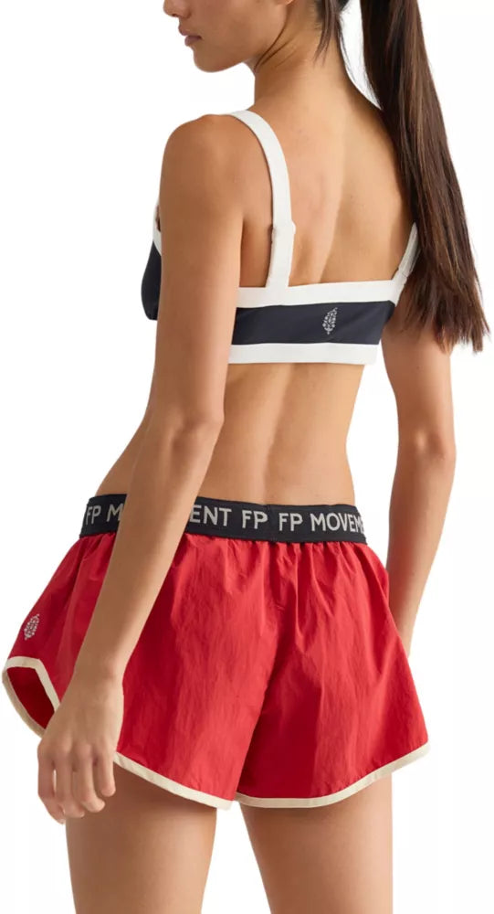 A woman wearing a black  top and red-colored athletic shorts with a black waistband that reads 'FP MOVEMENT'.
