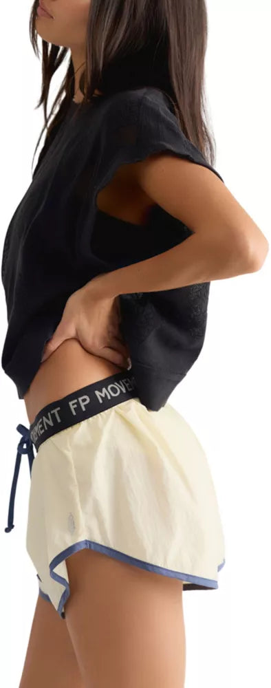 A woman wearing a black sleeveless top and cream-colored athletic shorts with a black waistband that reads 'FP MOVEMENT'.