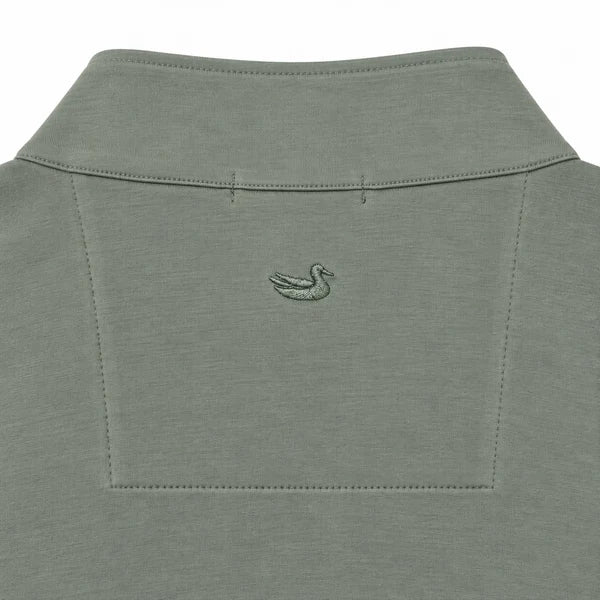 Close-up of the back of a muted sage green polo shirt, featuring a small embroidered duck logo centered below the collar.