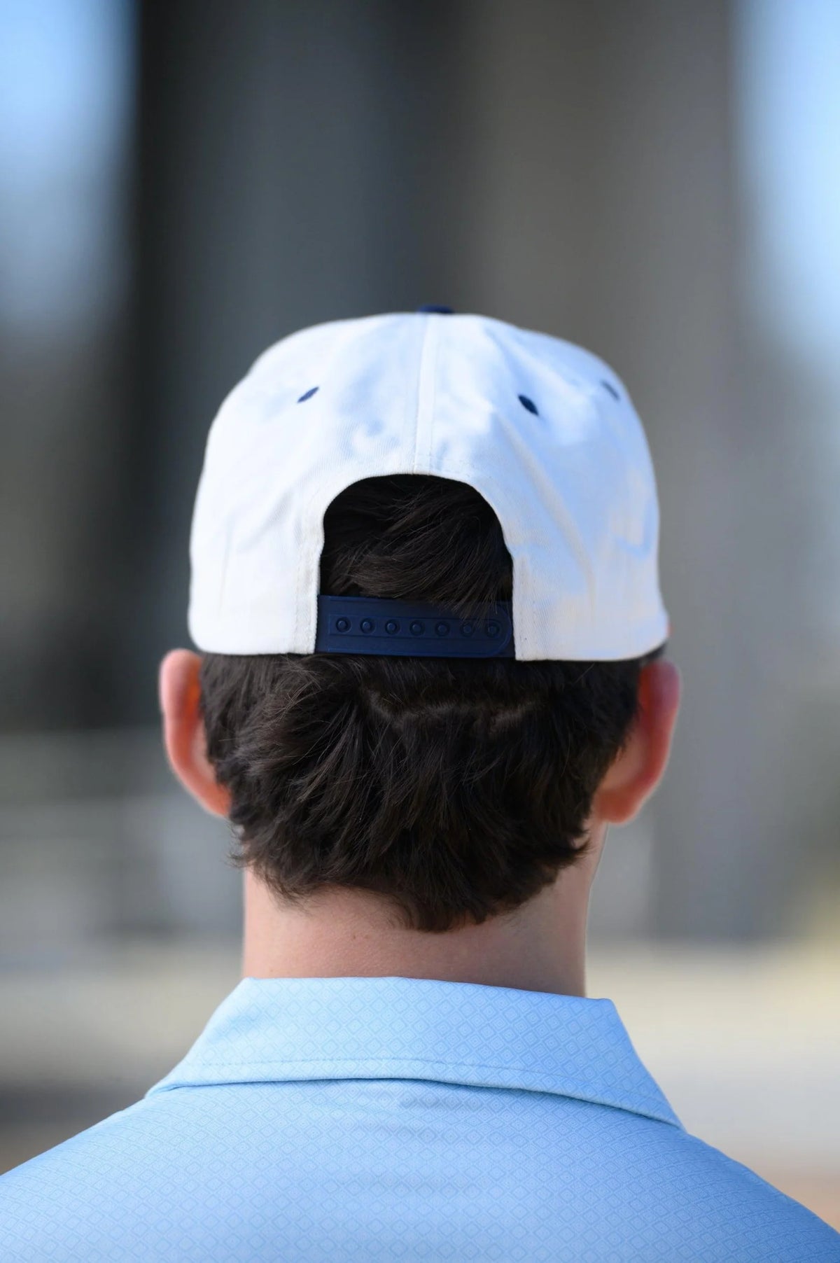 Person wearing a white cap with a blue logo, facing away from the camera.