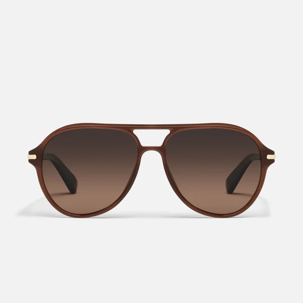 A pair of aviator-style sunglasses with a translucent brown frame and matching brown gradient lenses, featuring small gold metal accents on the temples, set against a light gray background.