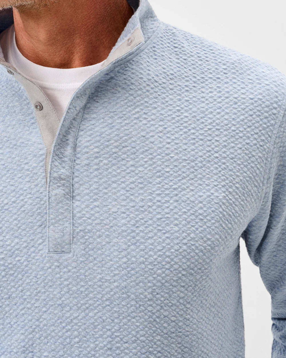 Close-up of a man wearing a light blue textured long-sleeve henley shirt over a white t-shirt, showing the collar and chest area.