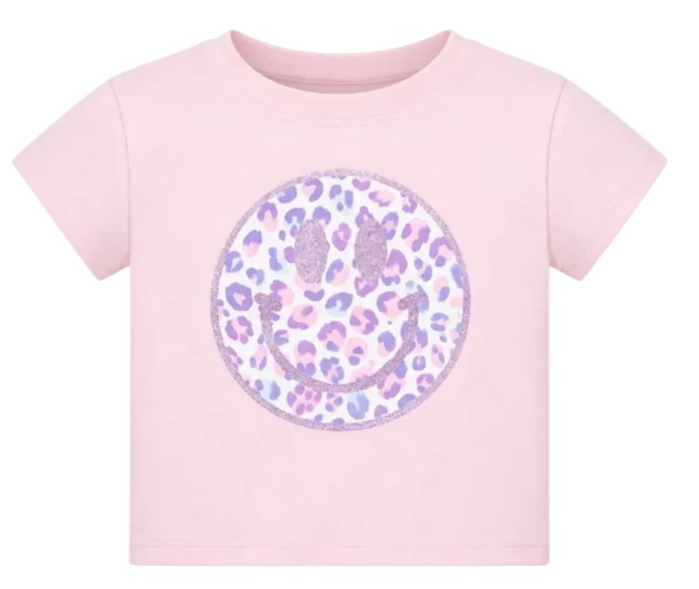 A light pink short-sleeve t-shirt featuring a large circular smiley face graphic on the front. The smiley face has a leopard print pattern in shades of purple, lavender, and pink on a white background, with a glittery pink border.