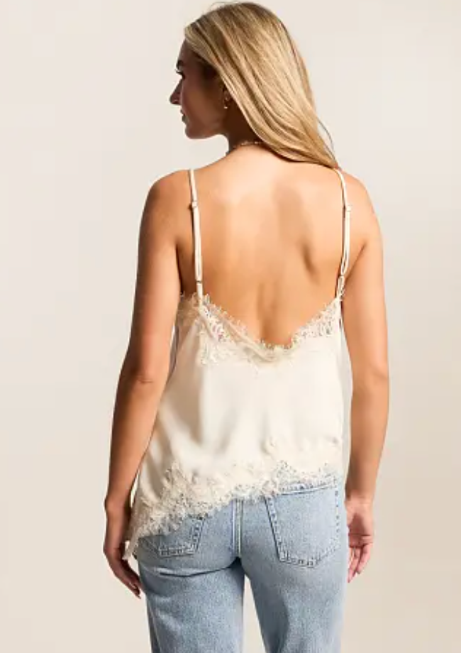 A woman shown from the back wearing a cream satin camisole top with lace trim and thin shoulder straps, paired with light blue jeans, against a plain light beige studio background.