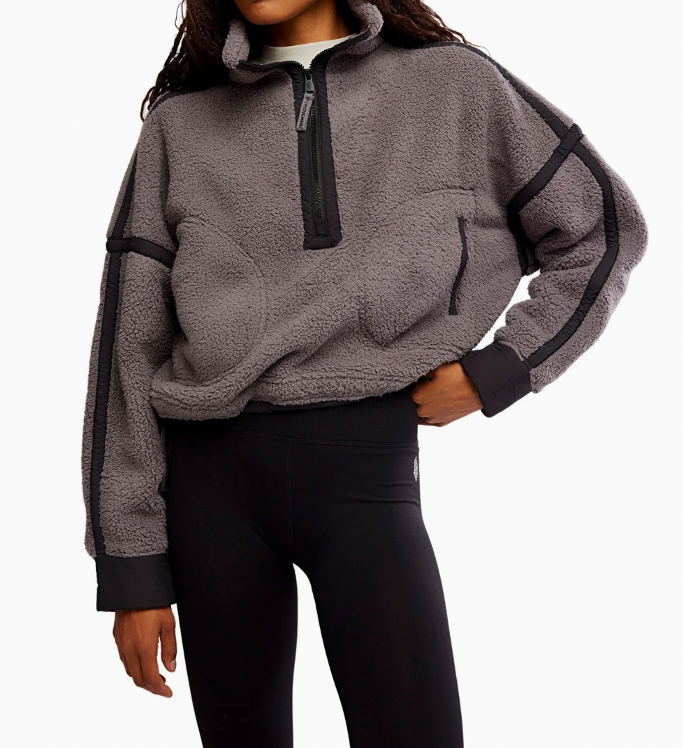 A woman wearing a gray sherpa fleece quarter-zip pullover with black contrast panels and black leggings, shown from the neck down against a plain white background.