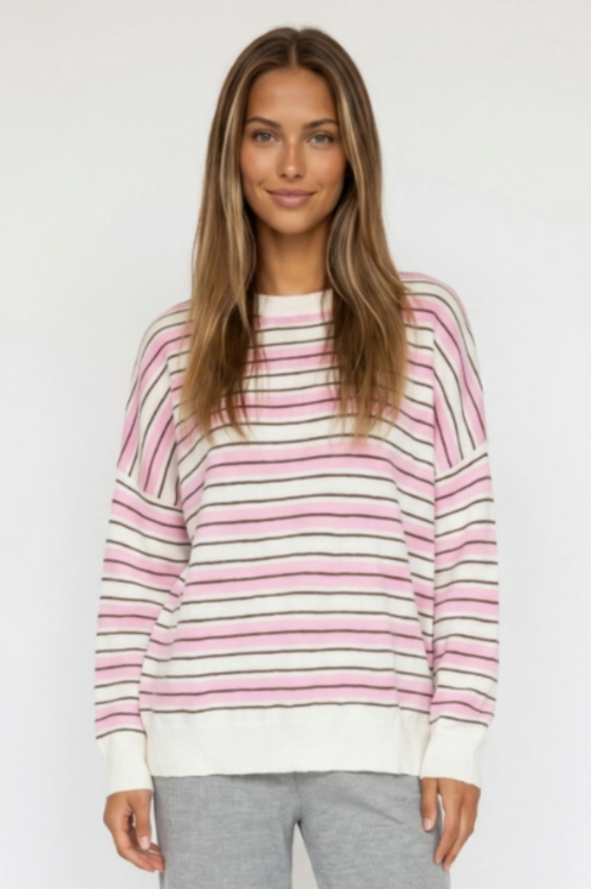 A woman modeling a pink, white, and black striped crewneck sweater against a plain white studio background.