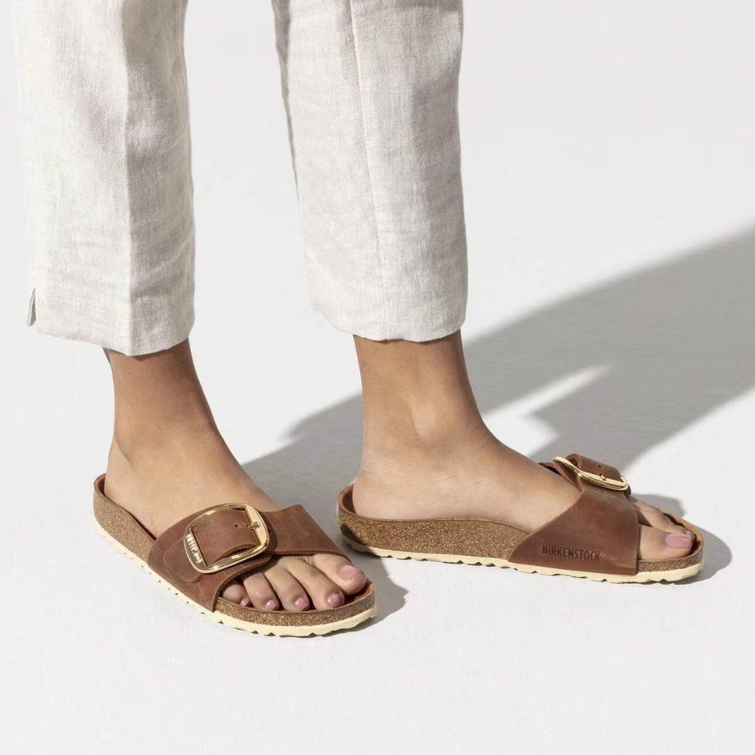 Brown sandals with gold buckles worn by a person on a white background