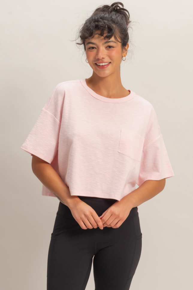 Woman wearing a light pink top and black pants against a plain background