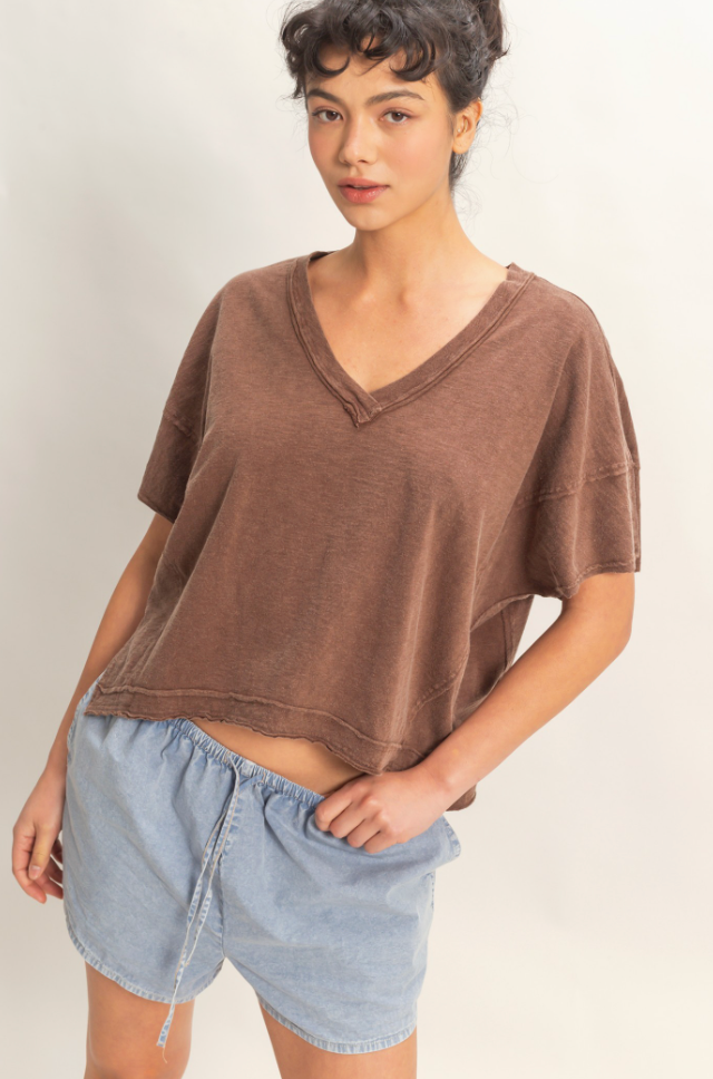 Woman wearing a brown oversized shirt and blue shorts on a plain background