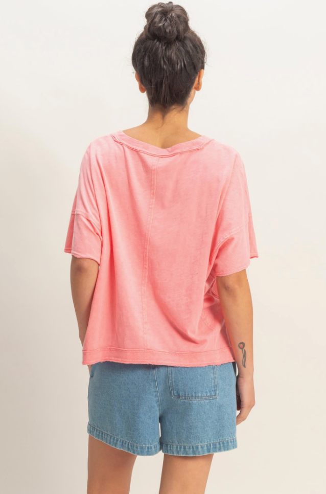 Person wearing a pink oversized shirt and blue shorts on a plain background