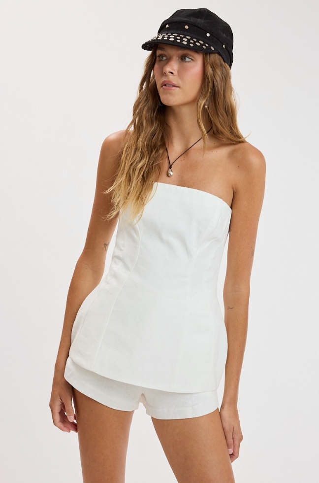 Woman wearing a white strapless top and shorts with a black cap on a white background