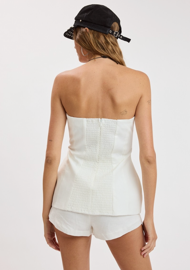 Person wearing a white strapless top and shorts with a black cap on a white background