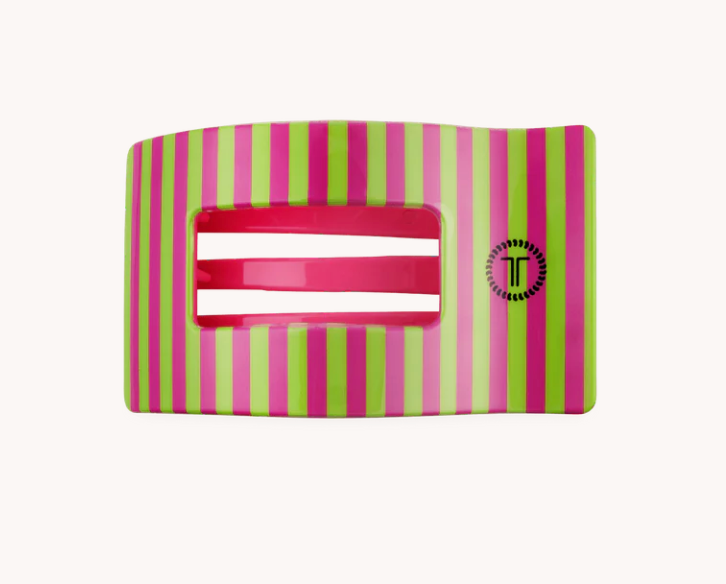 A rectangular hair claw clip with a glossy finish, featuring vertical stripes in lime green and magenta pink, with a central cutout showing two white horizontal bars inside, and a black circular logo with a stylized 'T' on the right side.