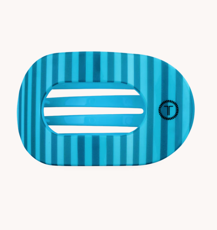 A blue striped hair claw clip with a central cutout and a small circular logo on the right side, set against a plain off-white background.