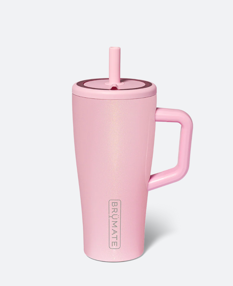 A pink insulated travel tumbler with a matching pink lid and straw, featuring a built-in handle and the vertical BRÜMATE logo near the bottom, shown on a light gray background.