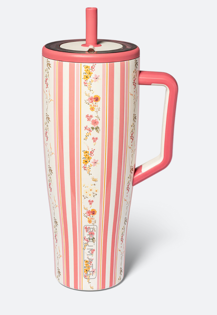 A tall travel tumbler with a pink handle, pink lid, and pink straw, decorated with vertical pink and cream stripes and delicate floral motifs, shown on a light gray background.