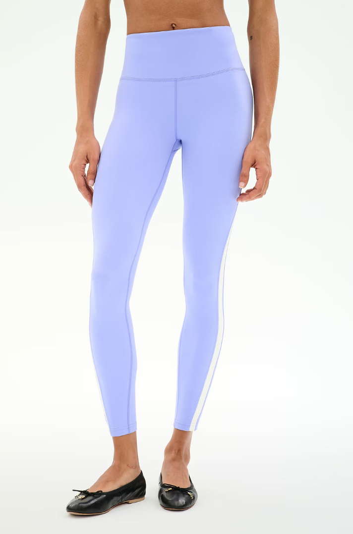 A model wearing light lavender high-waisted leggings with a white side stripe, paired with black flat shoes, against a plain white background.