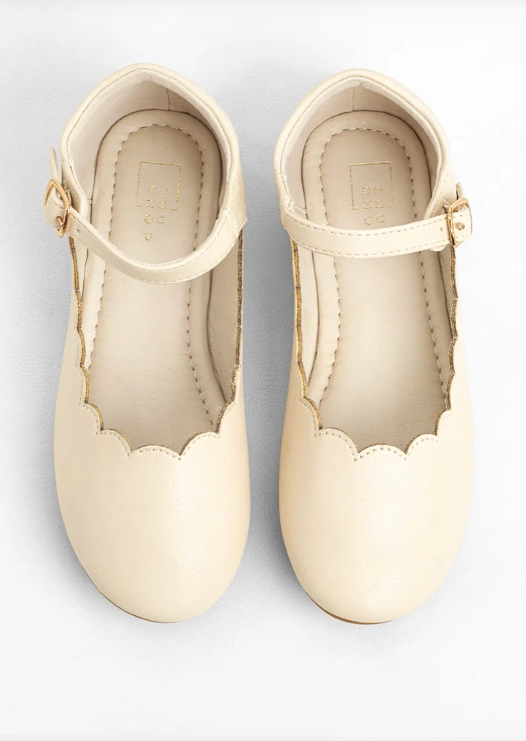 A pair of cream-colored faux leather Mary Jane shoes with scalloped edges and ankle straps, shown from a top-down view on a white background.