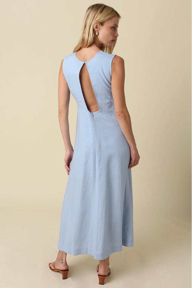 A woman modeling a sleeveless light blue maxi dress from the back, showing a large open back design, against a solid beige studio background.